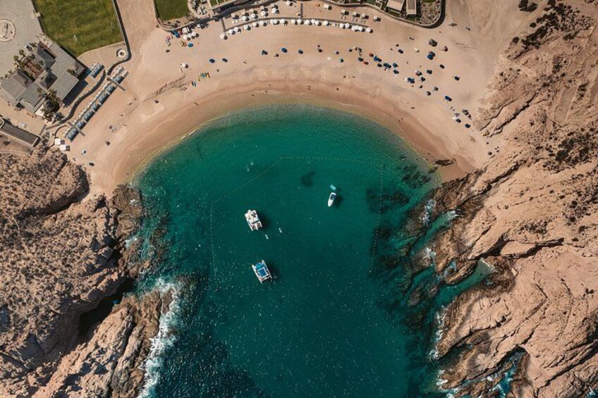 An aerial view of a coastal area with a beach, boats, and a resort with buildings and umbrellas. 1