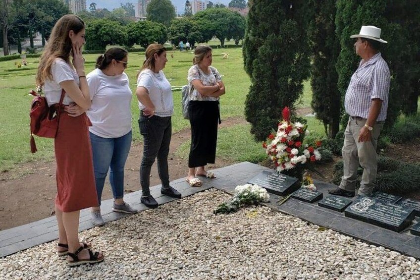 A memorial with engraved plaques, a floral arrangement, and a group of people standing around it. 1