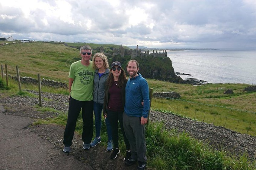 Un groupe de personnes se tient sur un sentier, avec un paysage côtier et un château en arrière-plan. 1