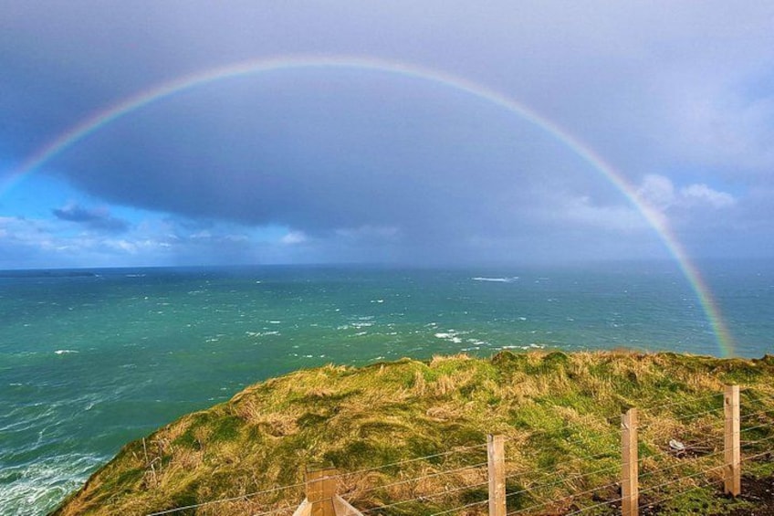 Un paysage côtier avec une falaise herbeuse, l’océan et un arc-en-ciel. 4