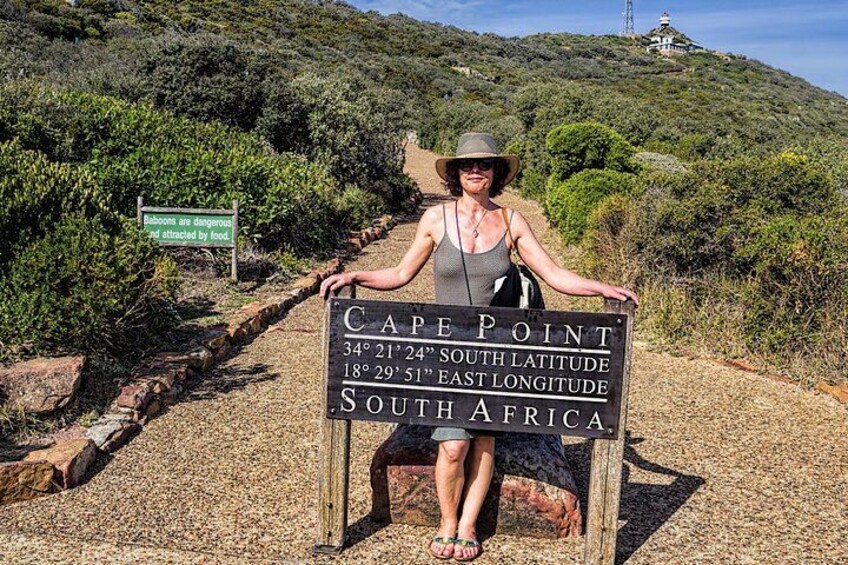 Une personne se tient derrière un panneau à Cape Point, en Afrique du Sud. Le panneau indique les coordonnées du lieu et contient un avertissement concernant la présence de babouins. 3