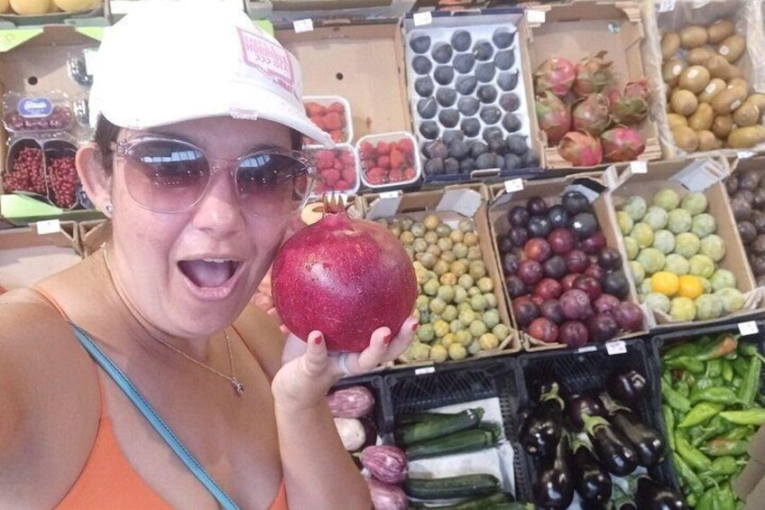 A person holding a pomegranate in a market with various fruits and vegetables on display. 3