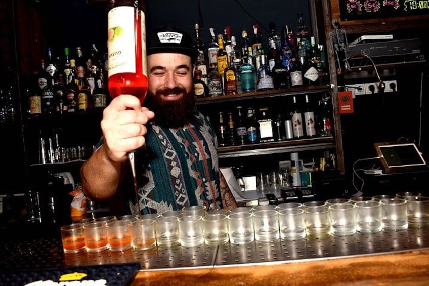 Ein Barkeeper hält eine Flasche, im Hintergrund eine Bar mit Flaschenregalen. 3