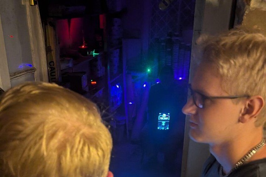 A person looking out a window at a dimly lit room with colorful lights and a neon sign. 4