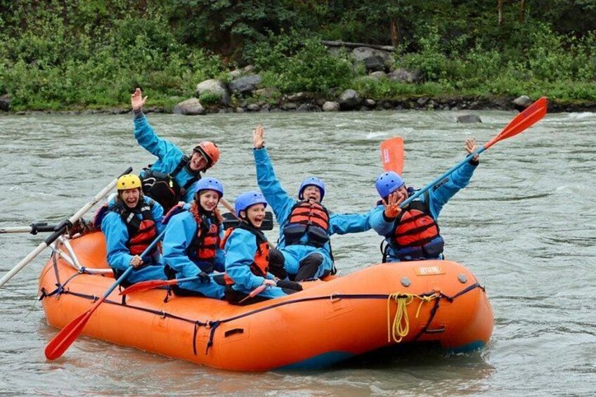 A group of people in an orange raft on a river surrounded by greenery. 4