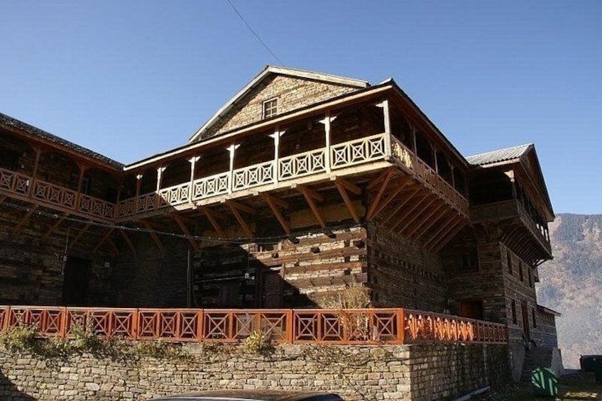 Een houten gebouw met een balkon, een stenen muur en bergen op de achtergrond. 4