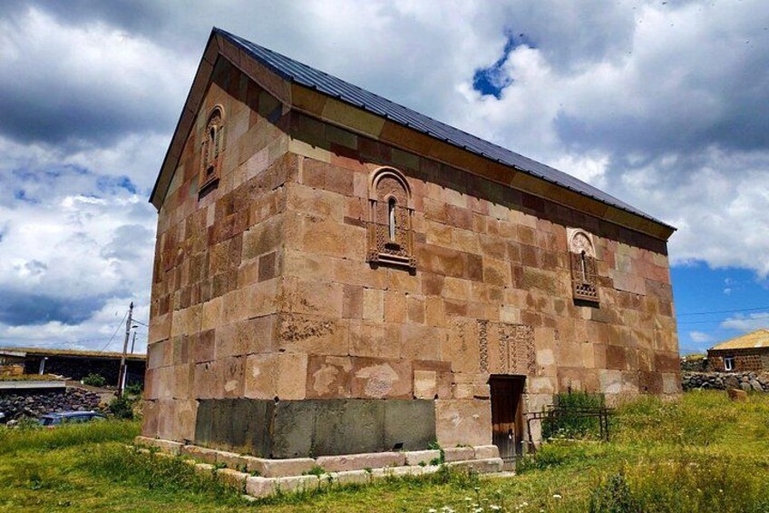 A stone building with a sloped roof, arched windows, and a small entrance. 5
