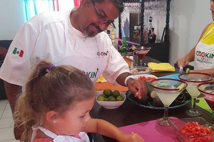 Een kok in een witte koksjas bereidt eten aan een tafel vol gerechten en ingrediënten. 4