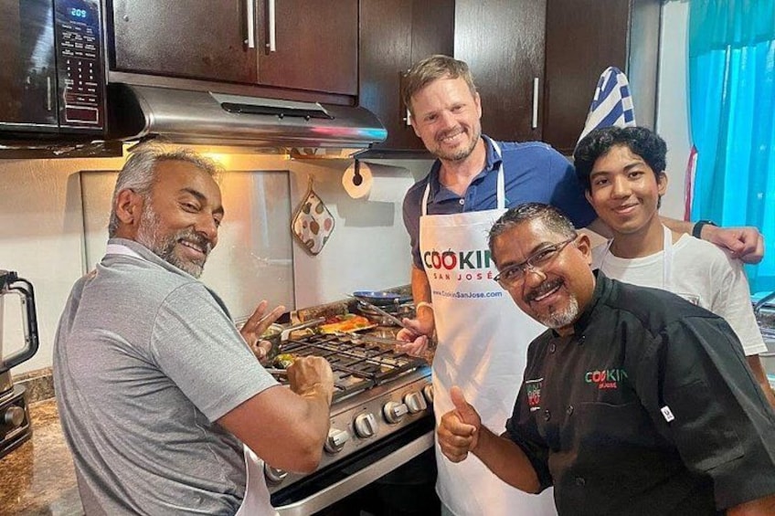 Een keuken met iemand die op een fornuis kookt, een andere persoon met een 'COOKIN' schort, en een kind op de achtergrond. 3