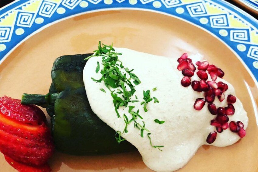 Grøn fyldt peberfrugt med hvid sauce og pynt af krydderurter og granatæblekerner, serveret på en tallerken med blå og gul mønstret kant. 3