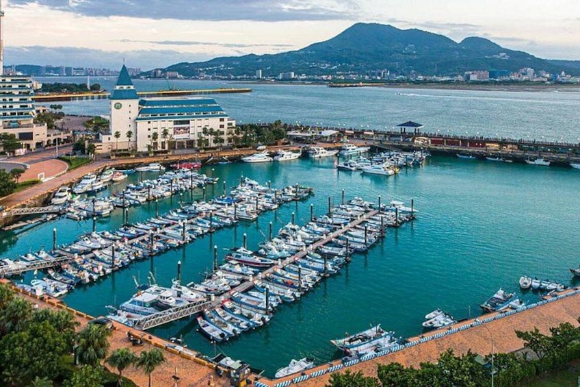 A marina with numerous boats docked, a coastal cityscape, and mountains in the background. 4