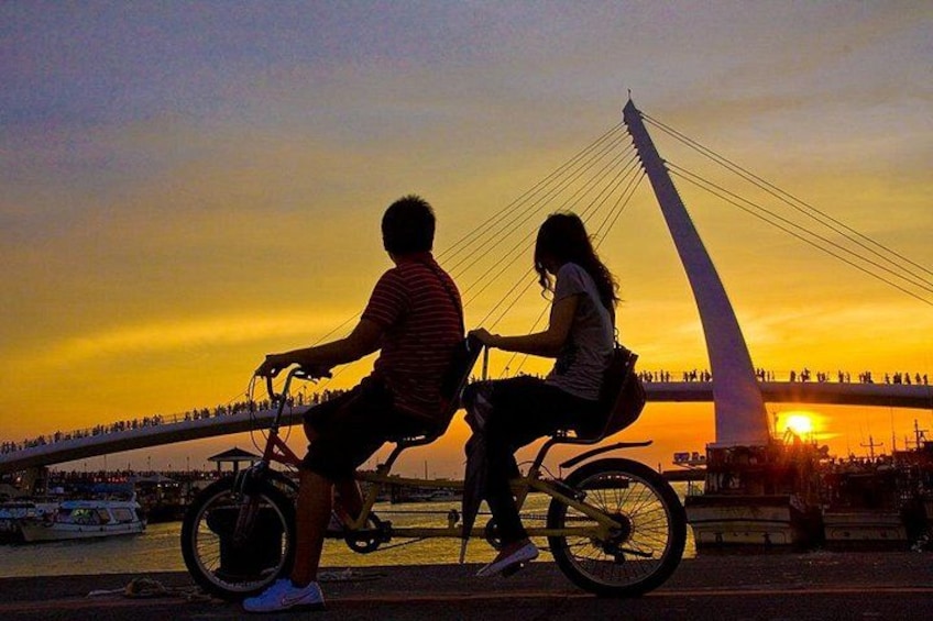 A sunset with a bridge and a couple on bicycles. 3