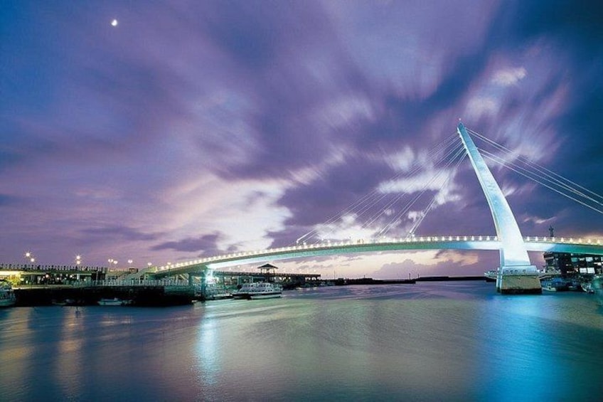 A bridge with a tall, white tower and cables, spanning over a body of water at night. 2