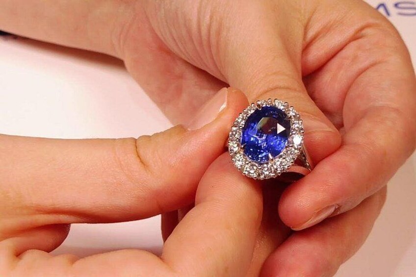 A hand holding a ring with a blue gemstone surrounded by smaller clear stones. 1