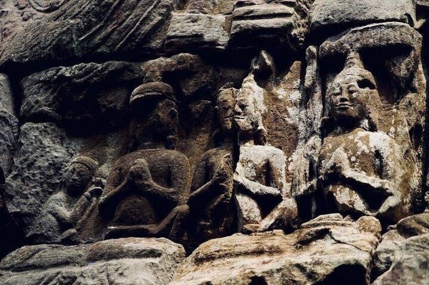 Ancient stone carvings of seated figures, possibly deities or historical figures, on a rocky surface. 4