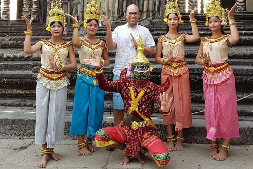 A group of people in traditional costumes, a performer in a red costume, and a temple structure in the background. 4