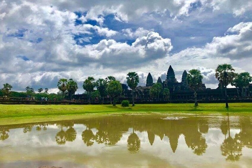 A temple complex with reflection in water, palm trees, and a cloudy sky. 3