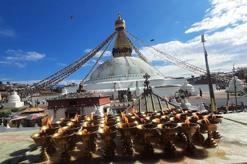 A large white stupa with a golden spire, surrounded by numerous brass lamps and a crowd of people. 4