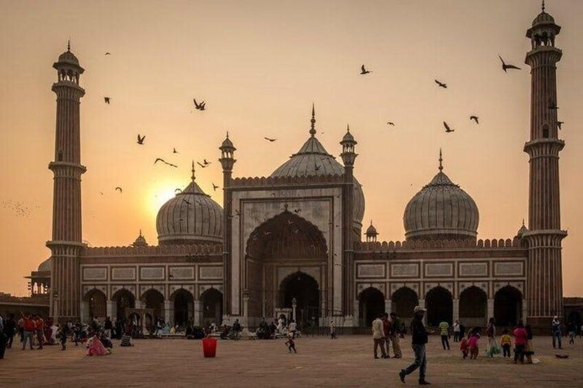 A large mosque with multiple domes and minarets, surrounded by people and birds. 2