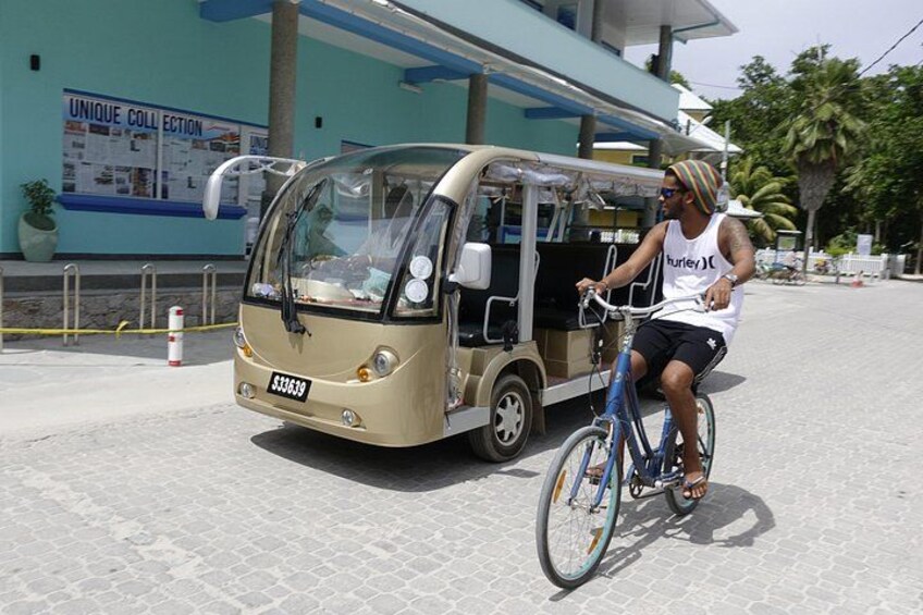 A person riding a bicycle next to a small, beige vehicle with a license plate. 5
