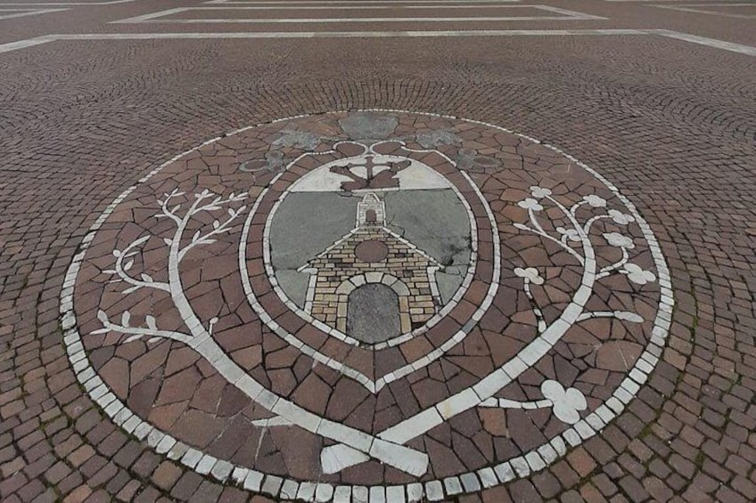 A circular mosaic with a central emblem surrounded by a brick pattern. 4
