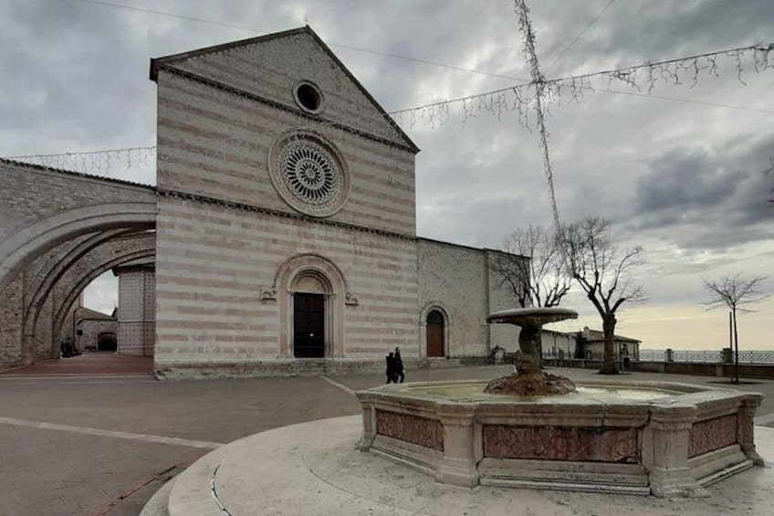A historic building with a large circular window and a stone fountain in the foreground. 3