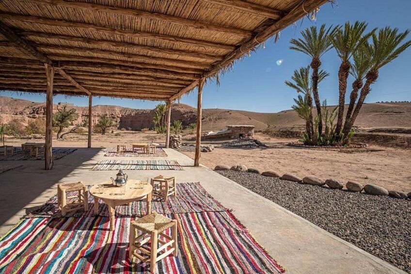 Un espace de restauration en plein air doté d’un toit de chaume, de tapis rayés aux couleurs vives et de palmiers. 3