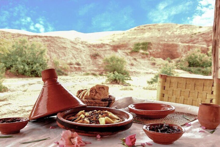 A traditional Moroccan meal setup with a tagine, bowls, and bread on a table in a desert landscape. 2
