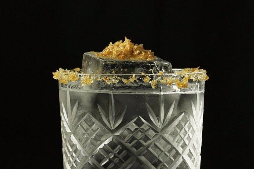 Un vaso transparente con un diseño geométrico, lleno de un líquido claro y decorado con un azúcar cristalizado. 2