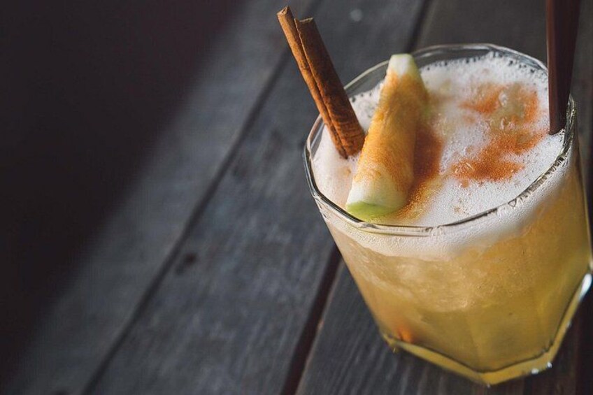 Un vaso con una bebida, una rama de canela y una rodaja de manzana sobre una superficie de madera. 3