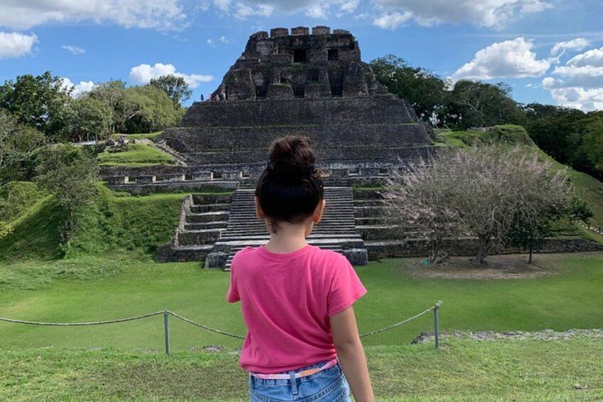 A person in a pink shirt standing in front of a large ancient pyramid structure. 1