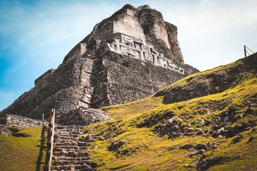 A large stone pyramid with inscriptions, a staircase leading up to it, and a grassy hill in the foreground. 1