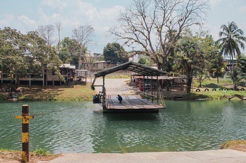 A wooden dock extending over a calm river, surrounded by trees and a small building. 3