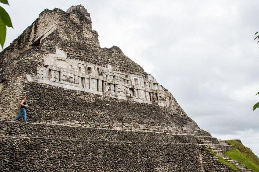 An ancient pyramid with stone carvings, a person walking on the side, and a cloudy sky. 2
