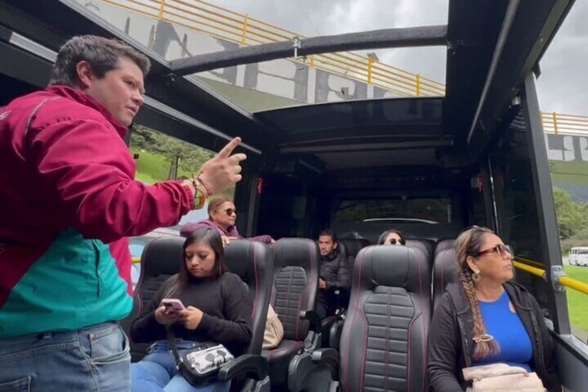 A bus interior with passengers seated and a person standing at the front. 2