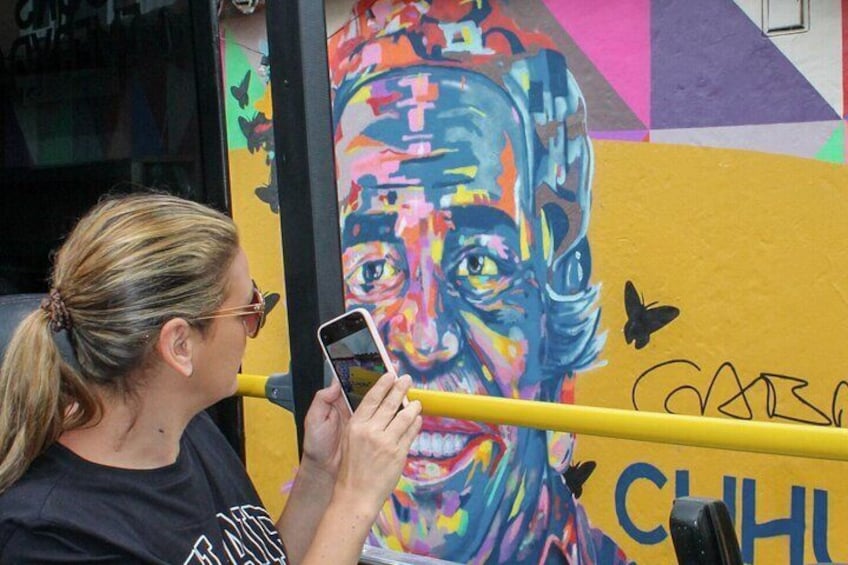 A person taking a photo of a colorful mural with a yellow railing. 1