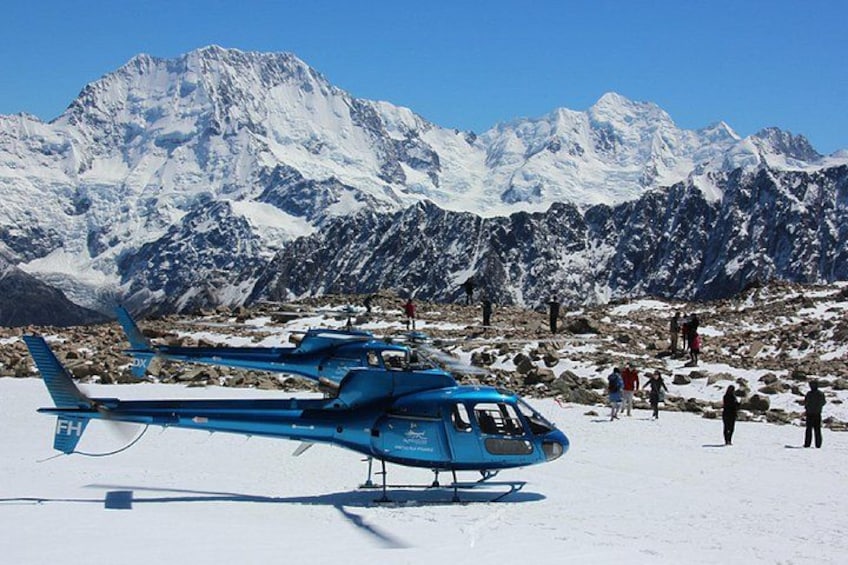 A blue helicopter on a snowy mountain with people in the background. 1