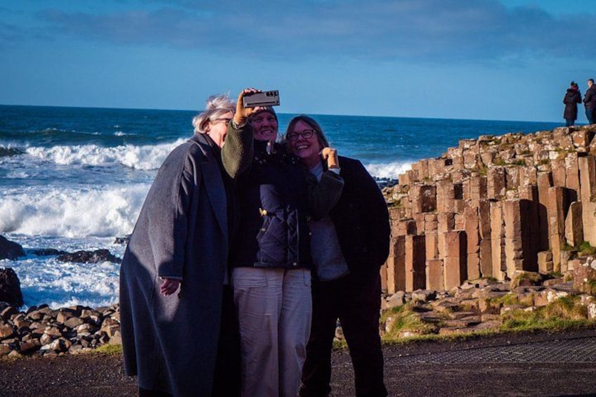 Three people standing near a coastal stone structure with waves in the background. 3