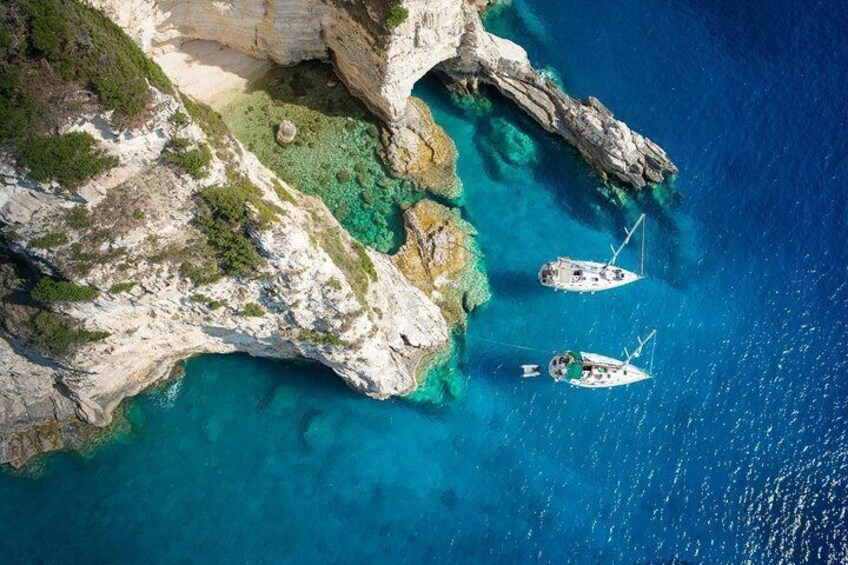 An aerial view of a coastal area with clear turquoise waters, rocky cliffs, and two boats anchored near the shore. 3