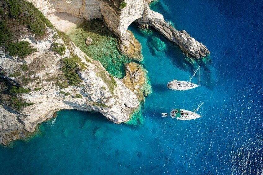 A coastal landscape with rocky cliffs and clear blue waters. There are two boats anchored near the shore. 2