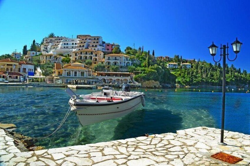 A boat docked at a pier with a stone walkway, a lamp post, and a hillside town in the background. 1