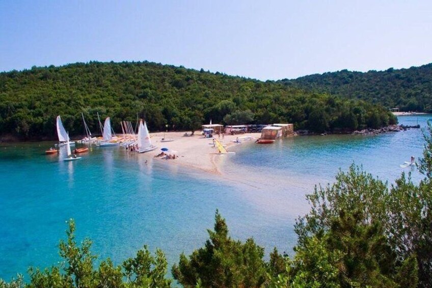 A coastal area with sailboats, a sandy beach, and a forested hill. 2