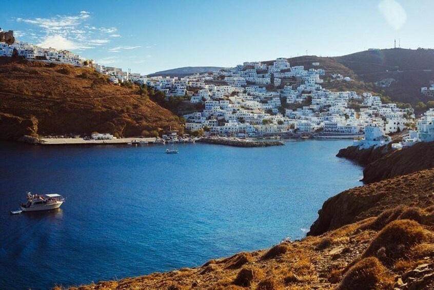 A coastal town with white buildings on a hillside, a body of water, and a boat. 2