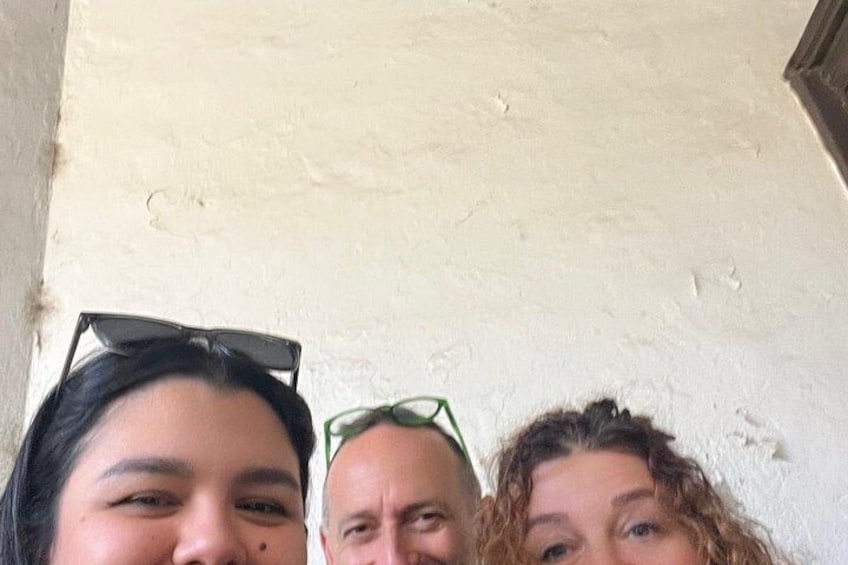 Three people standing close together, with a textured wall in the background. 2