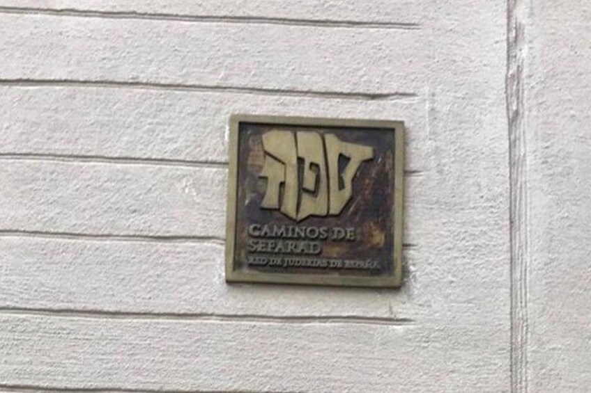 A weathered metal plaque with the inscription 'CAMINOS DE SEELARAD' mounted on a white wall. 1