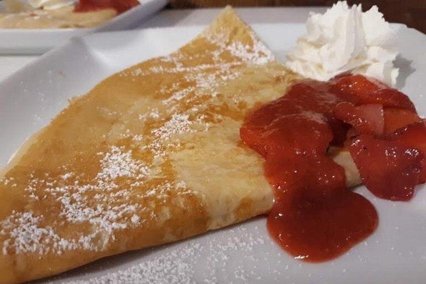 A crepe with powdered sugar and strawberry sauce on a white plate. 2
