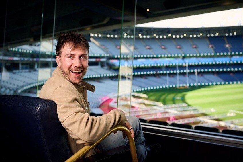 Een persoon zittend op een tribune met uitzicht op lege tribunes en een sportveld. 2