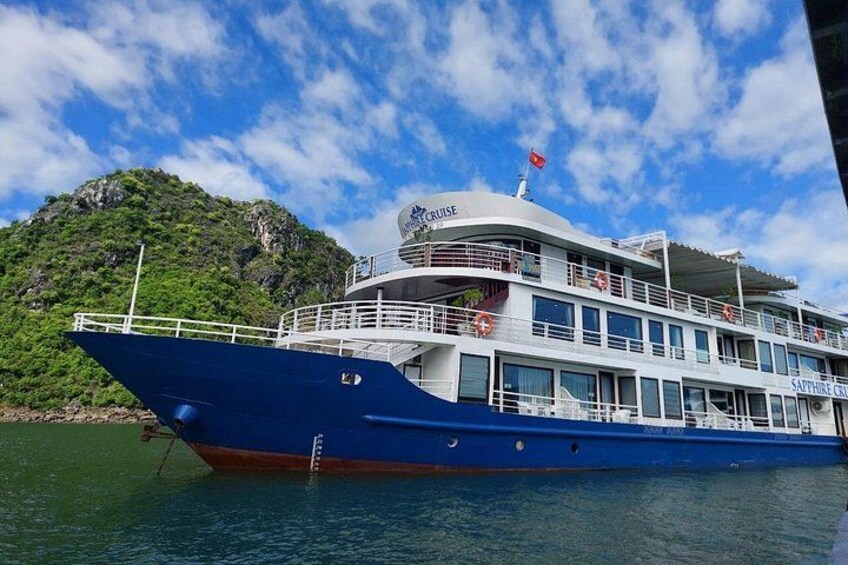 A large blue cruise ship with multiple decks, a flag, and a mountainous backdrop. 1