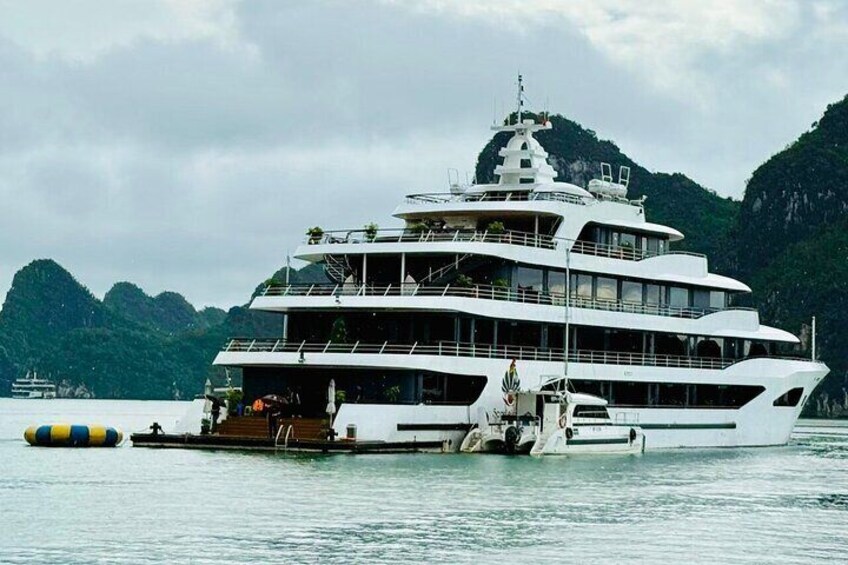 A large white cruise ship docked at a port with lush green hills in the background. 2