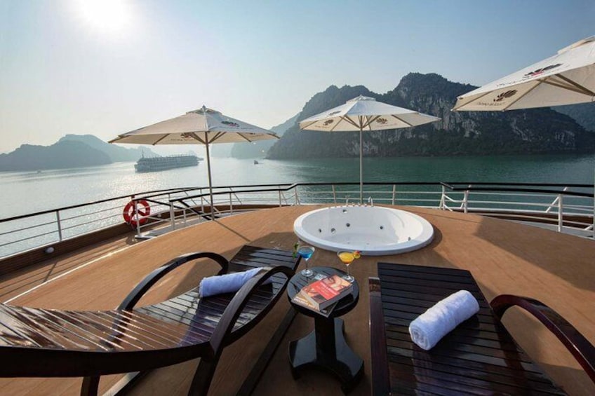 A deck with lounge chairs, a hot tub, and umbrellas overlooking a body of water with mountains in the background. 3